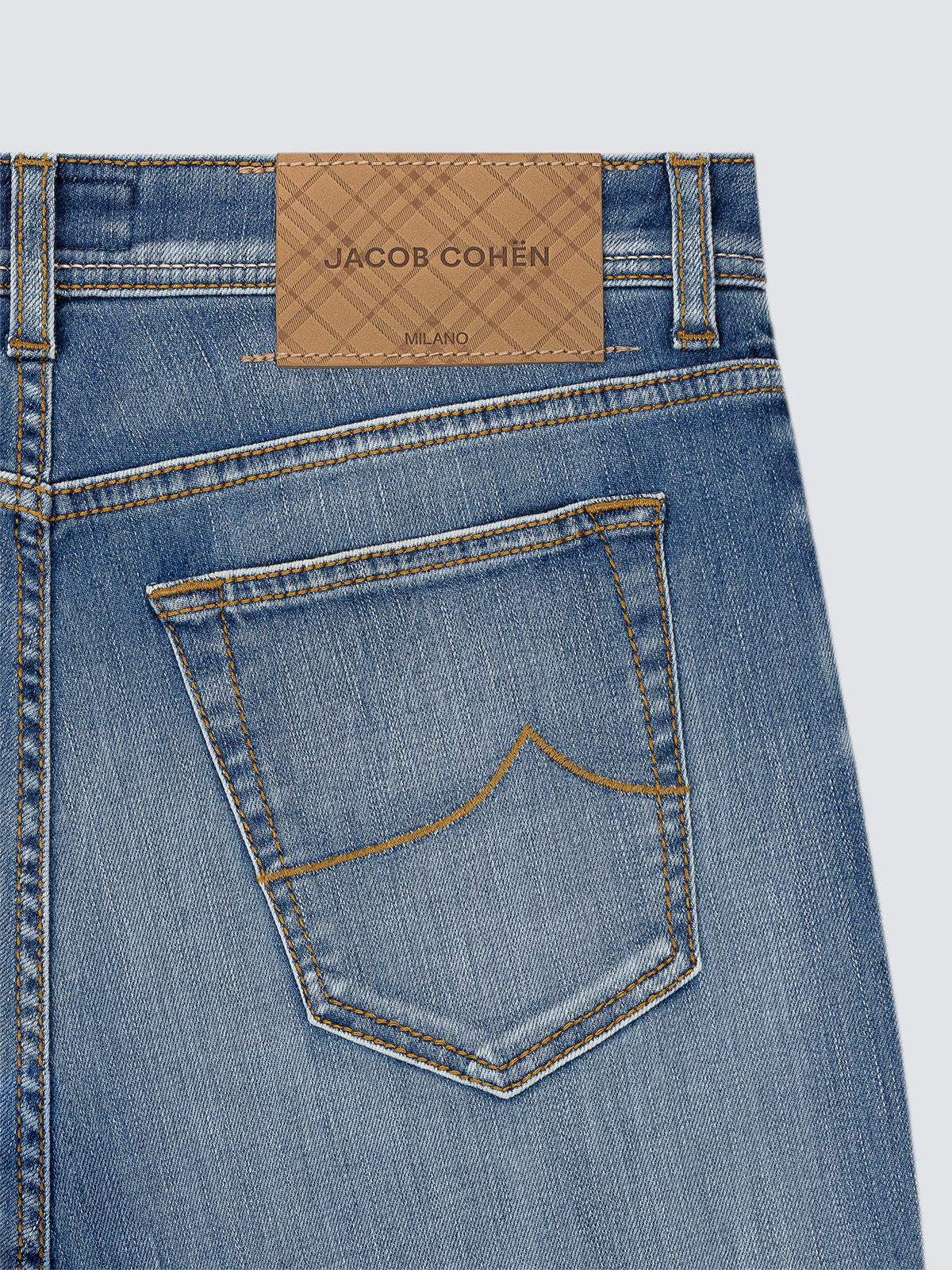 Close-up of blue jeans with a Jacob Cohen label on a light gray background