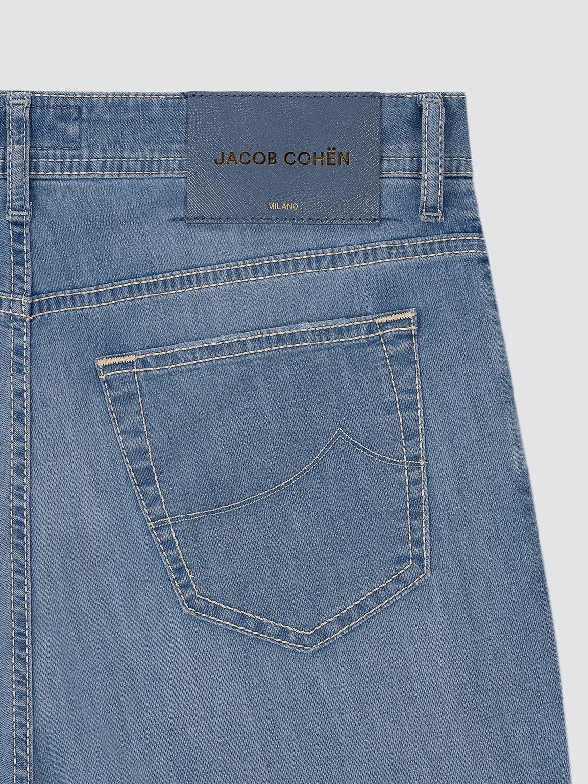 Close-up of blue denim jeans with a Jacob Cohen label on a light gray background