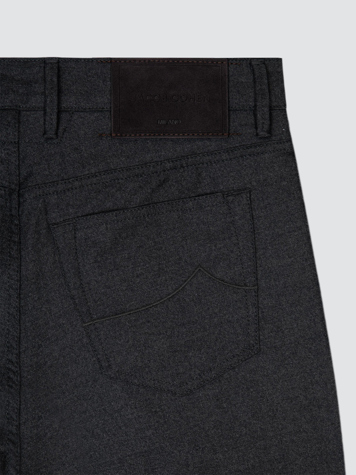 Close-up of the back waistband and pocket area of dark charcoal gray wool 5 pockets pants Jacob Cohën, showing belt loops, a dark leather patch, and stitching on a light gray background.