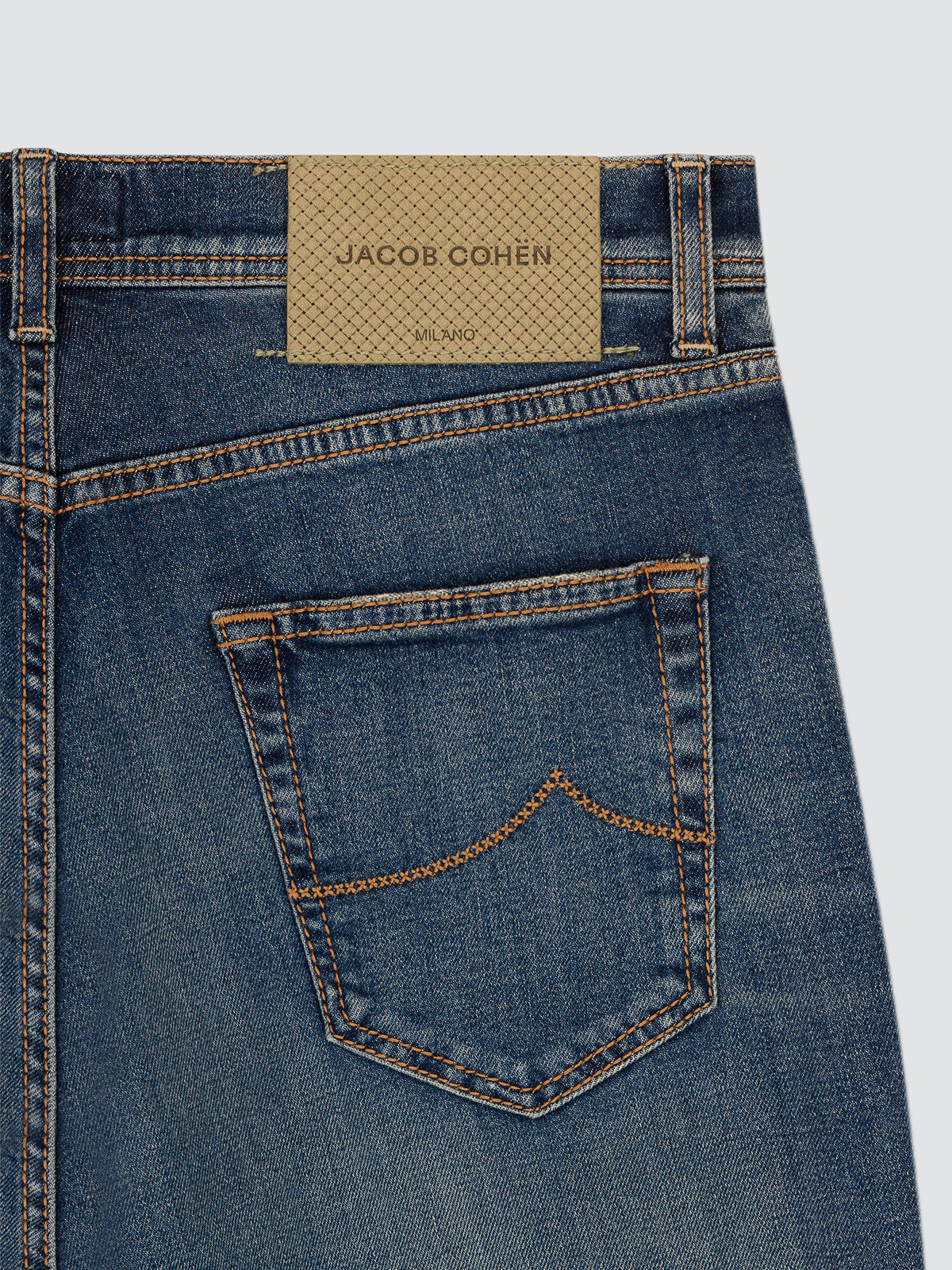 Close-up of the back waistband and pocket area of blue denim jeans with a tan woven jacquard label reading JACOB COHEN.