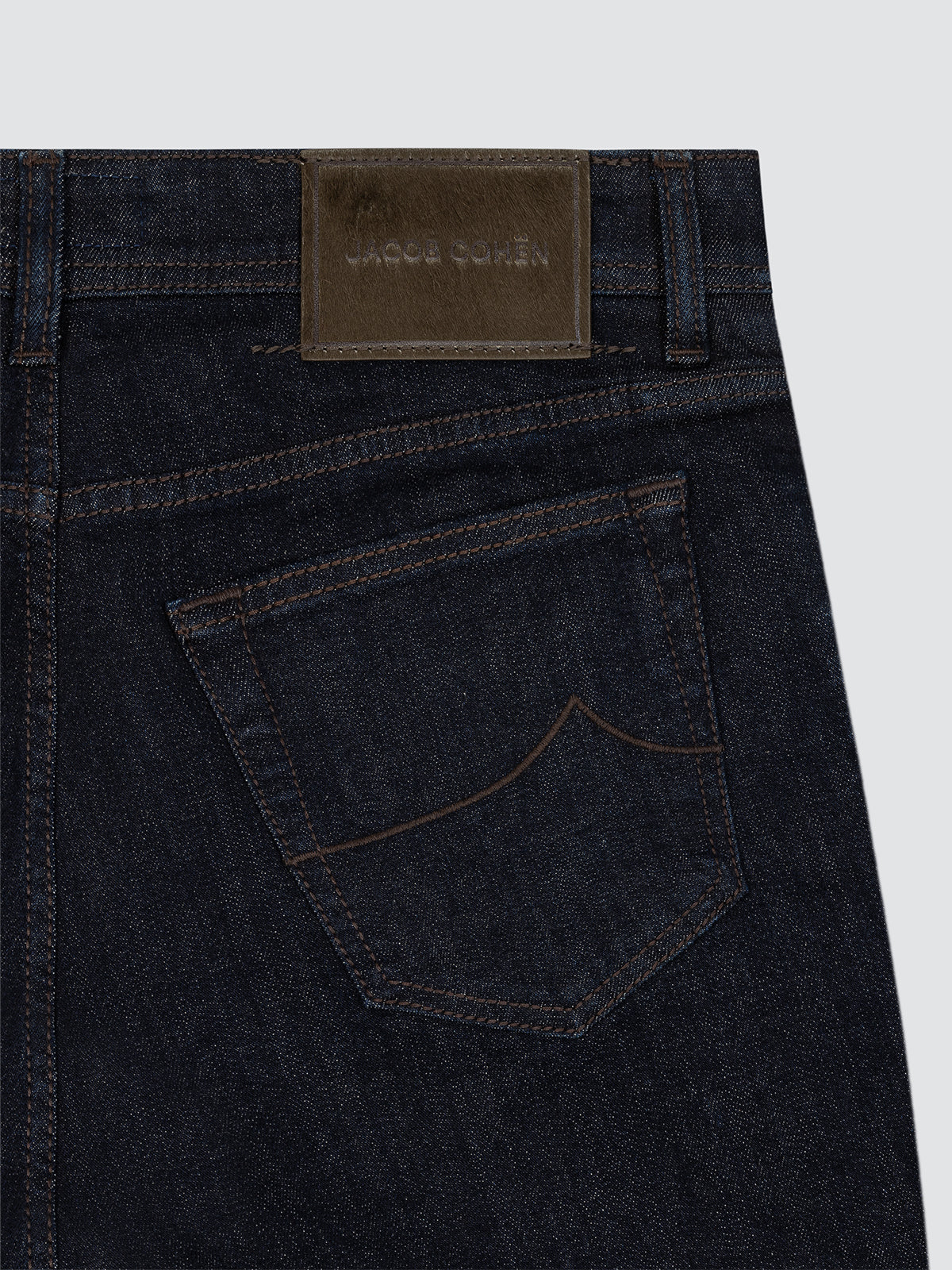 Dark blue jeans with a brand label on a light gray background by Jacob cohen back view