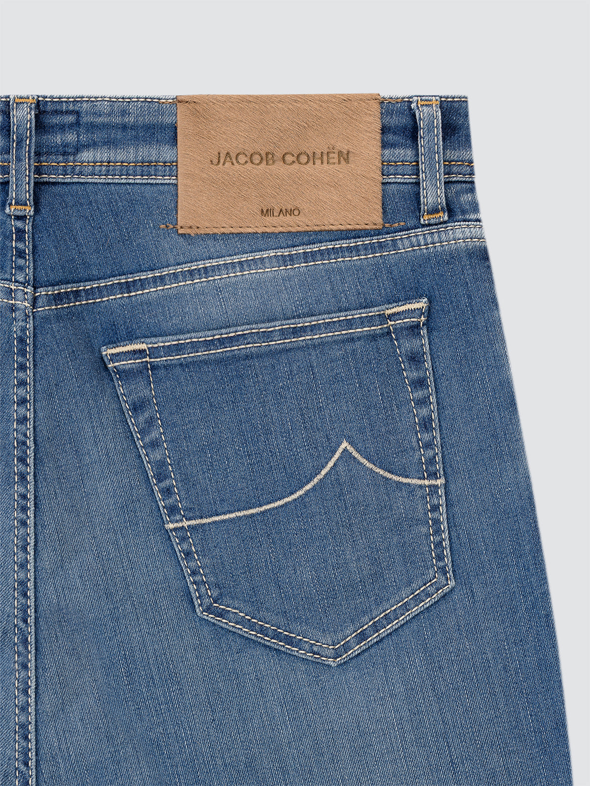 Close-up of blue jeans with a Jacob Cohen label on a light gray background