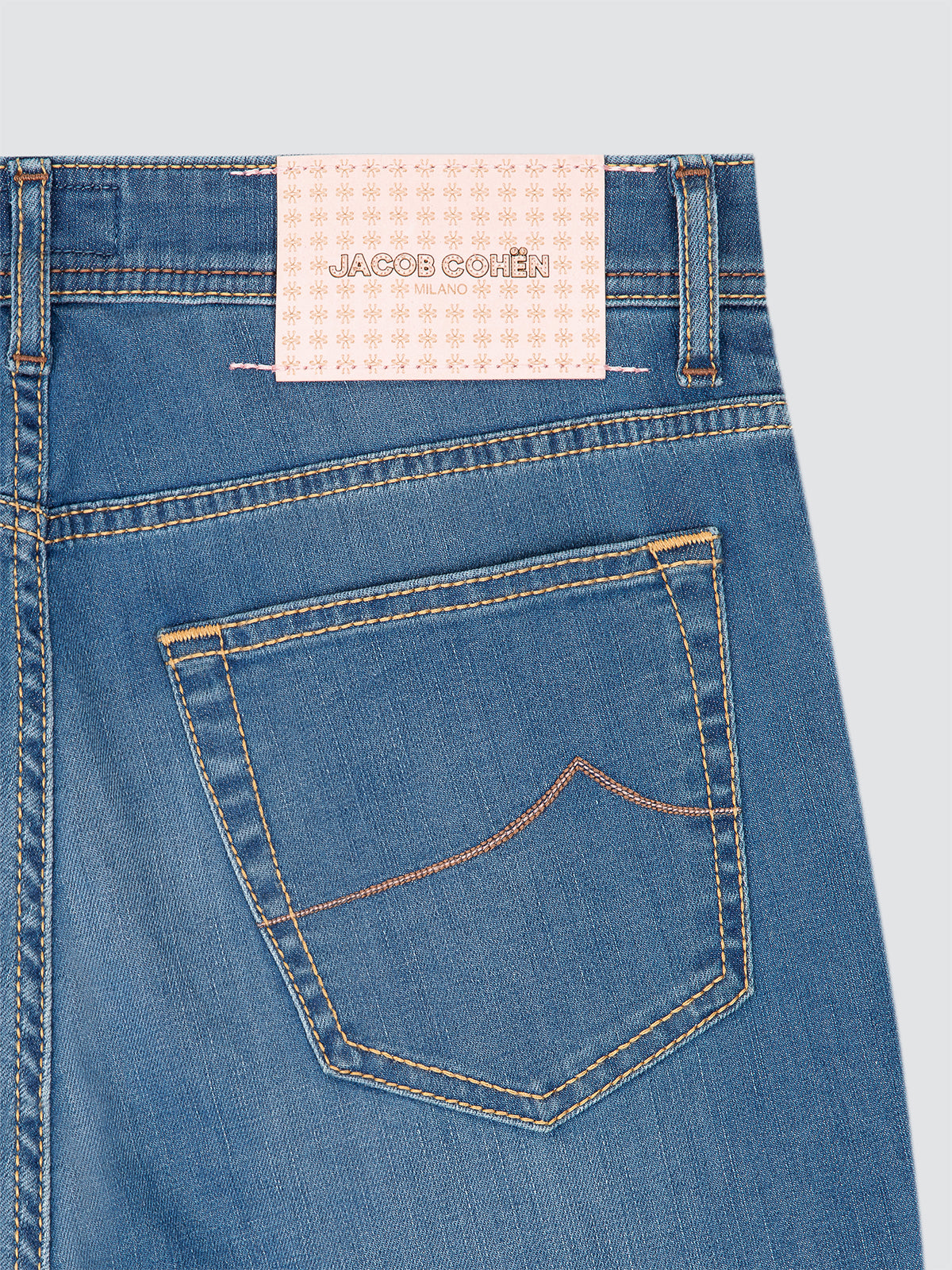 Close-up of blue jeans with a Jacob Cohen label on a light gray background