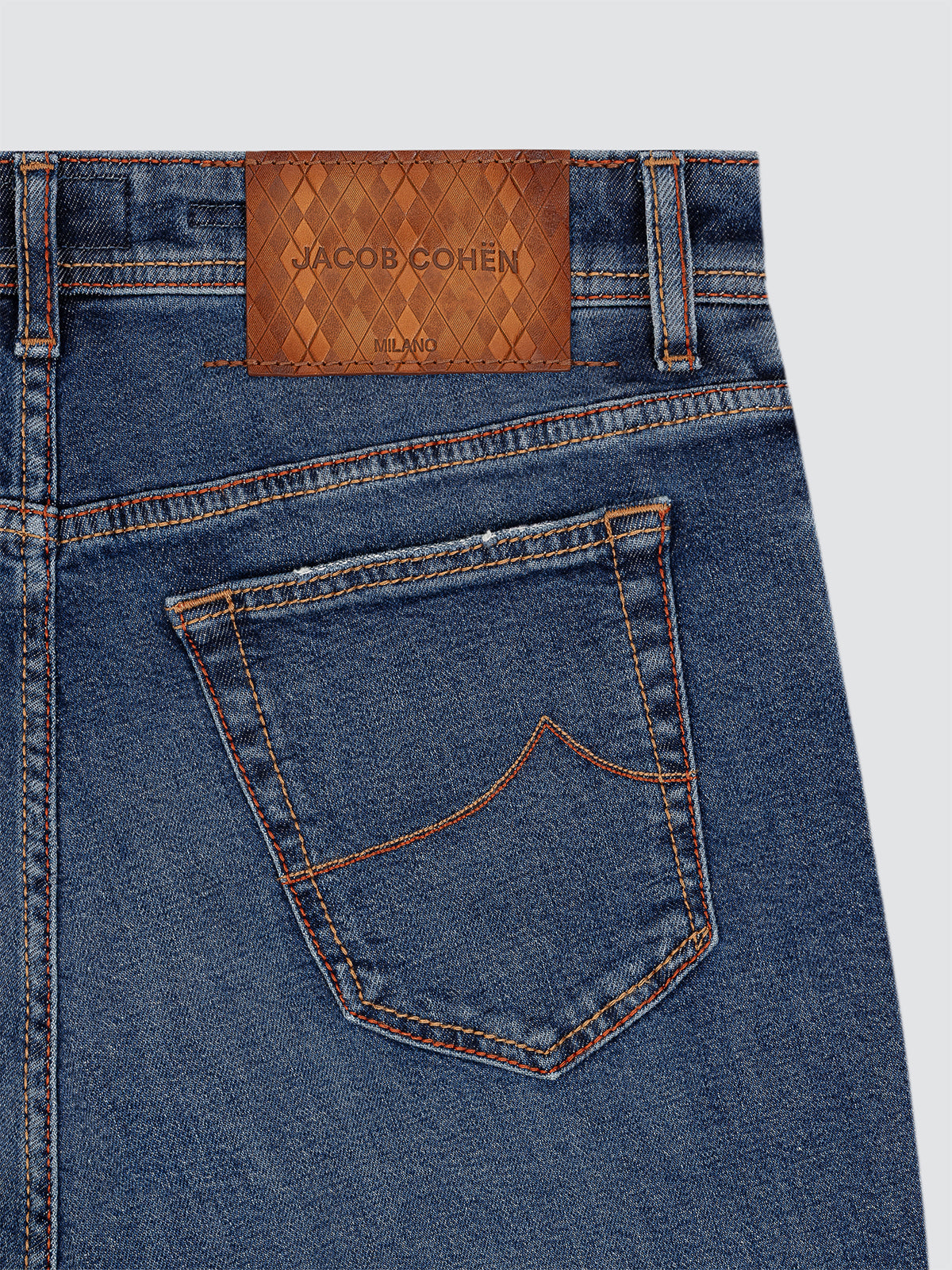 Close-up of blue jeans with a Jacob Cohen label on a light gray background