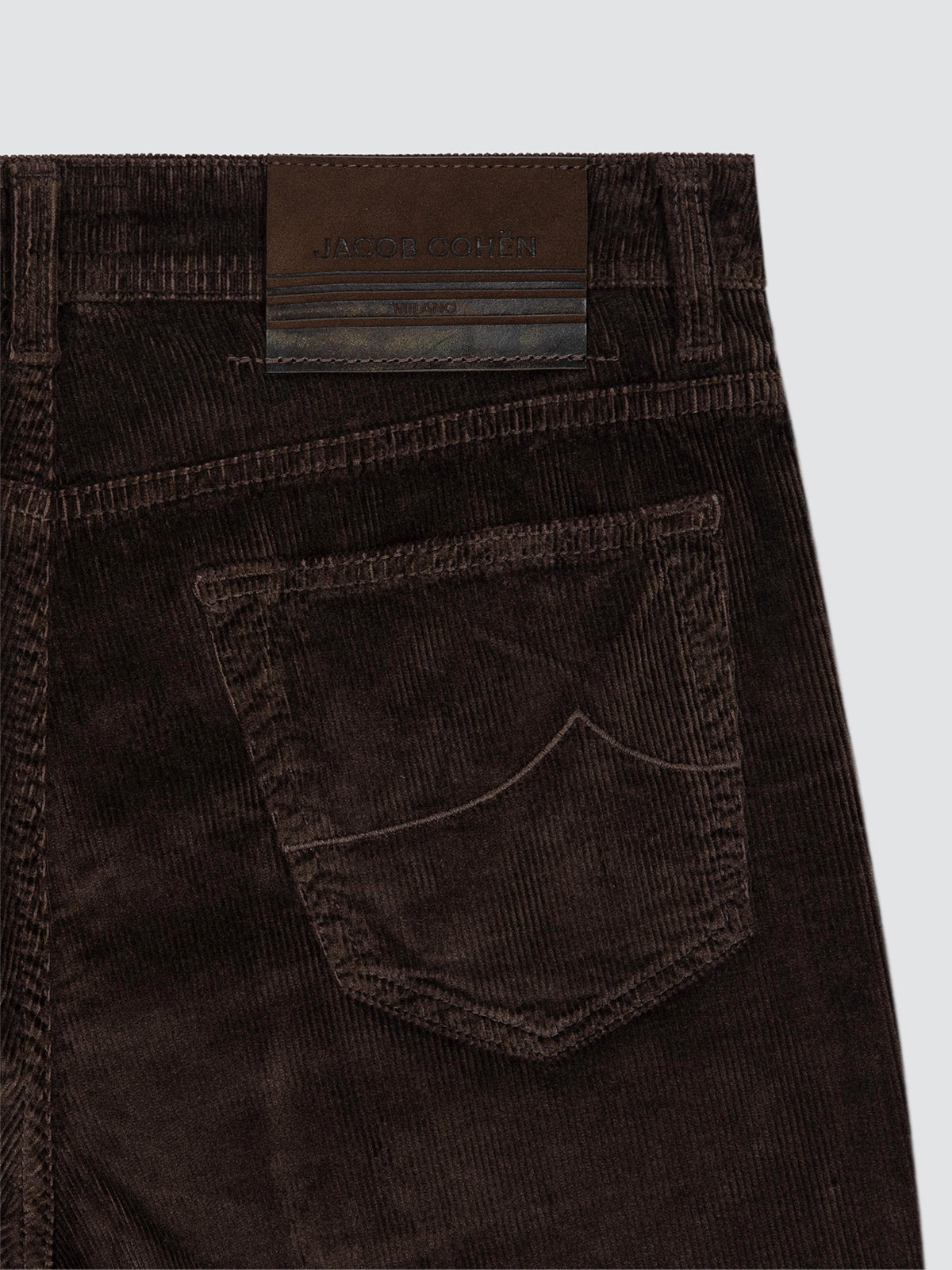 Close-up of the back waistband and pocket of dark brown corduroy jeans, showing a brown leather patch with the brand name JUNIOR AESTHETIC.