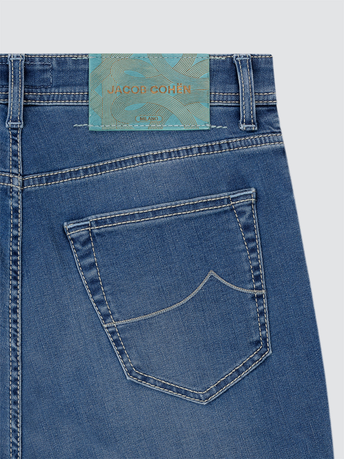 Close-up of blue jeans with a brand Jacob Cohen nick-slim label on a light gray background