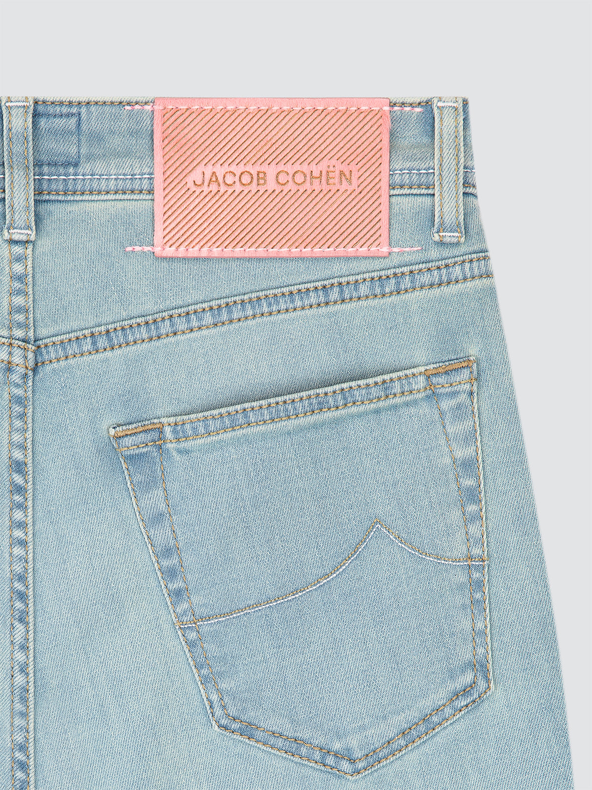 Light blue denim jeans with a pink Jacob Cohen label on a light gray background