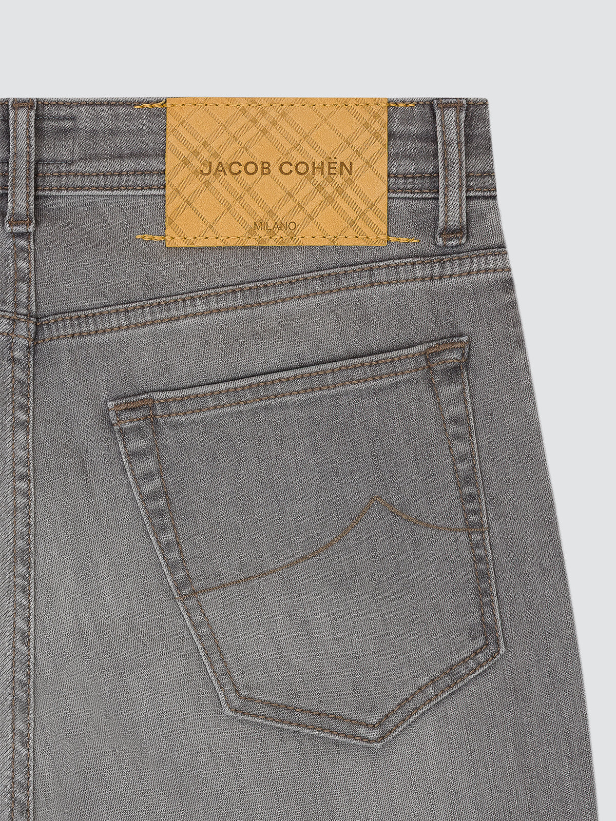 Close-up of the back waistband and pocket of gray denim jeans with a tan leather patch reading JACOB COHËN MILANO.