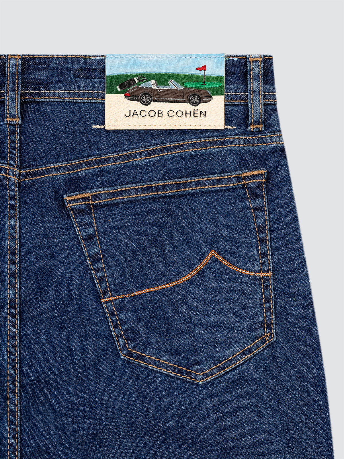 Close-up of blue jeans with a Jacob Cohen patch with Porsche and golf on a light gray background