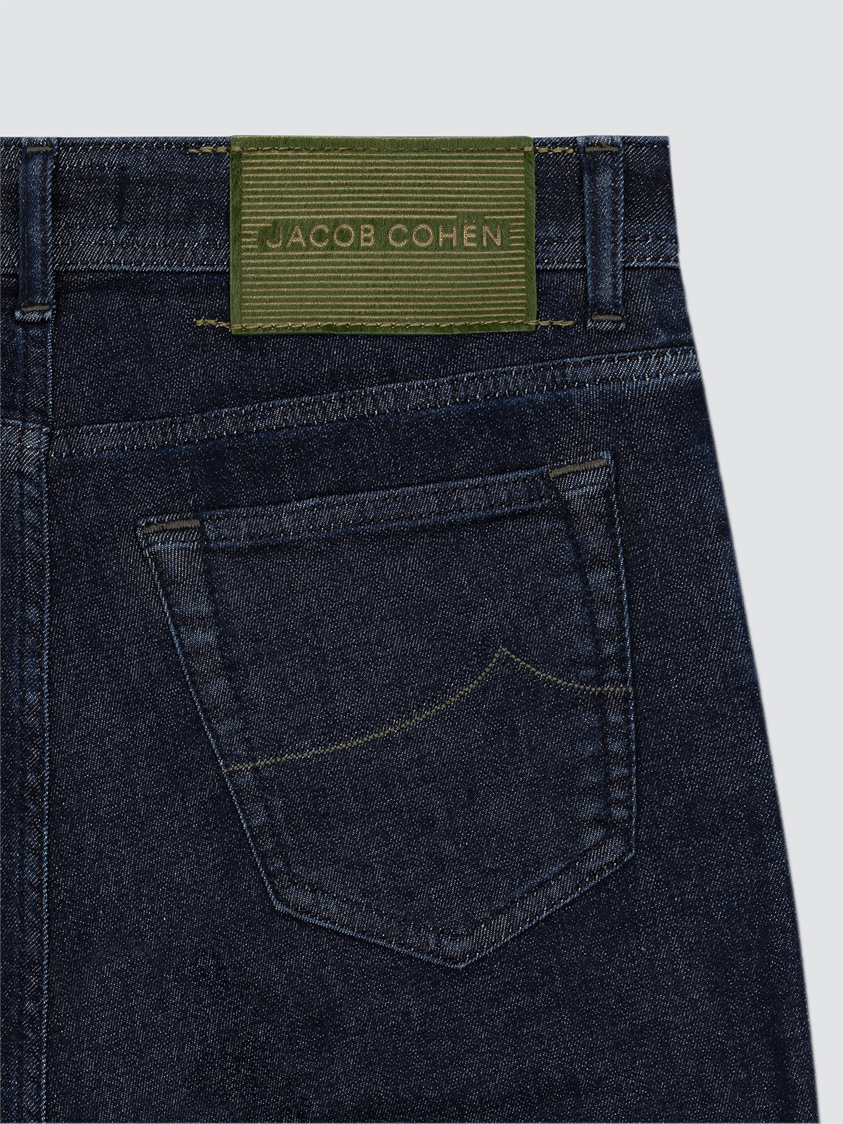 Close-up of dark blue jeans with a Jacob Cohen label on a light gray background