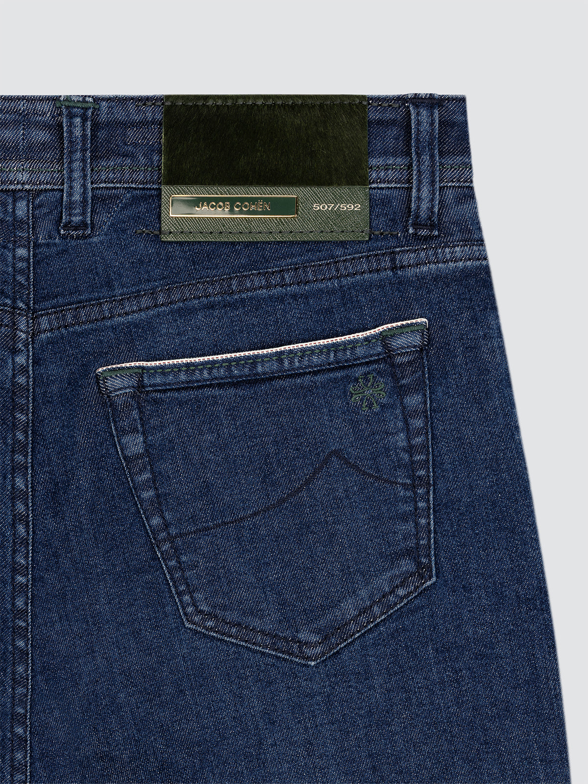 Close-up of blue jeans limited edition with a brand green Jacob Cohën label on a light gray background