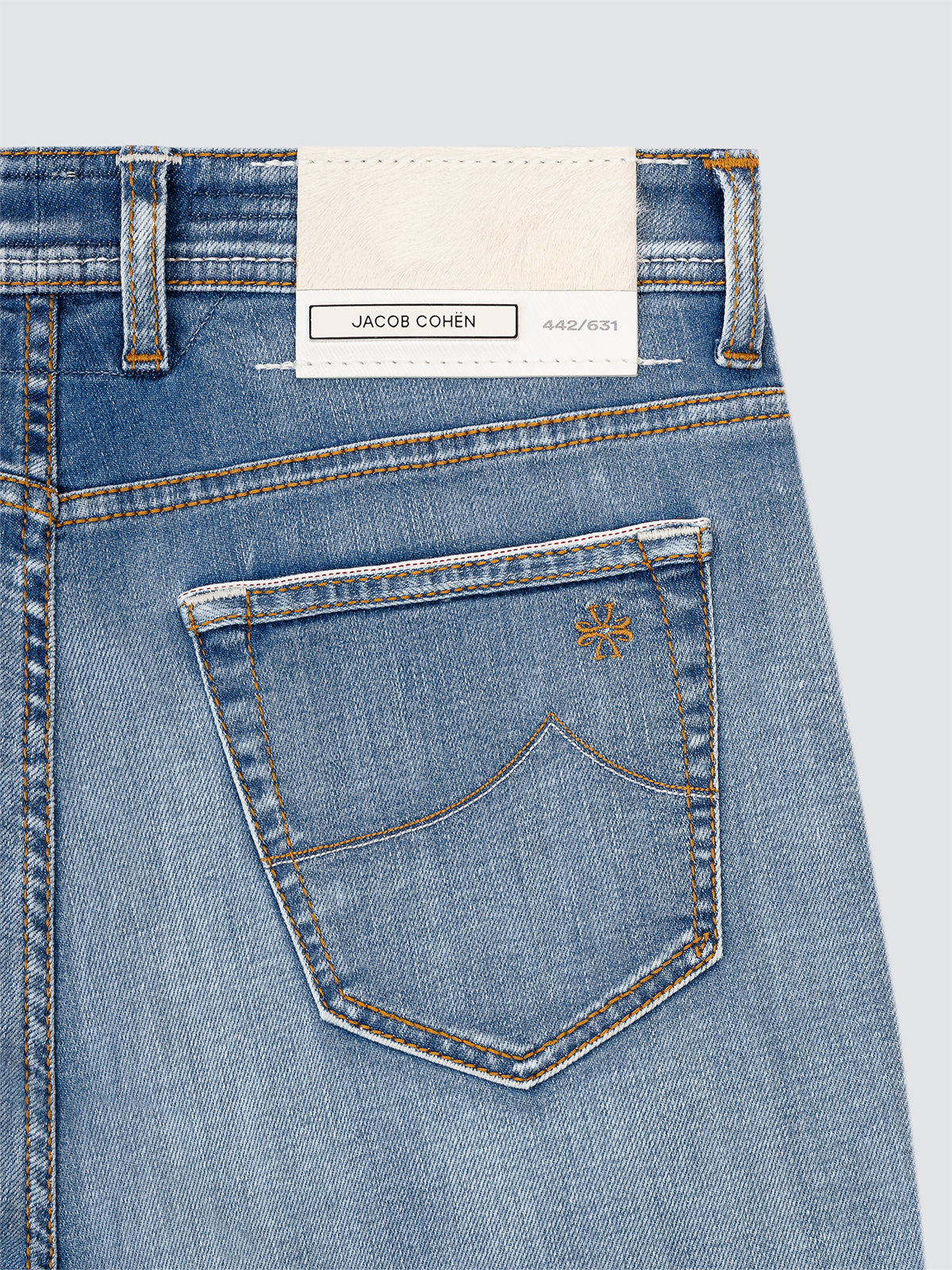 Close-up of blue jeans with a brand label JACOB COHEN LIMITED on a light gray background