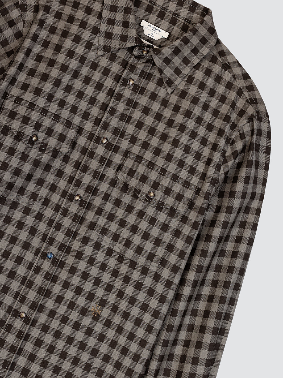 Close-up of a brown and gray checkered shirt with a brand label on a light gray background
