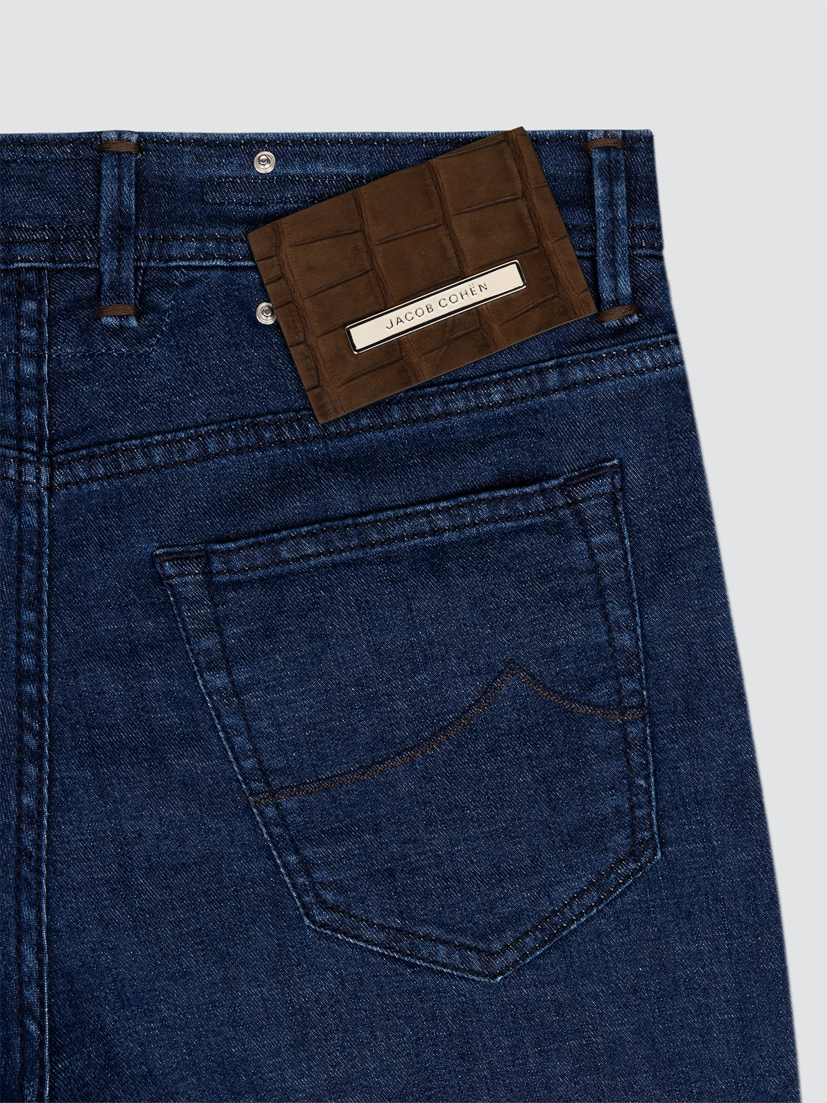 Close-up of blue jeans Jacob Cohen  with a brown Crocodile leather patch and visible brand name on a light gray background