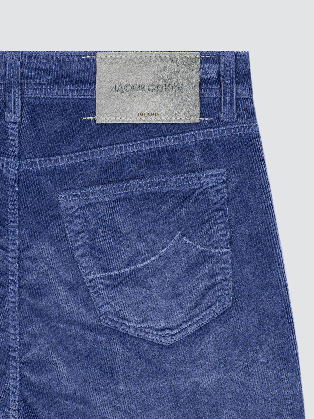 Blue corduroy pants lavender brand label Jacob Cohën back patch on a light gray background