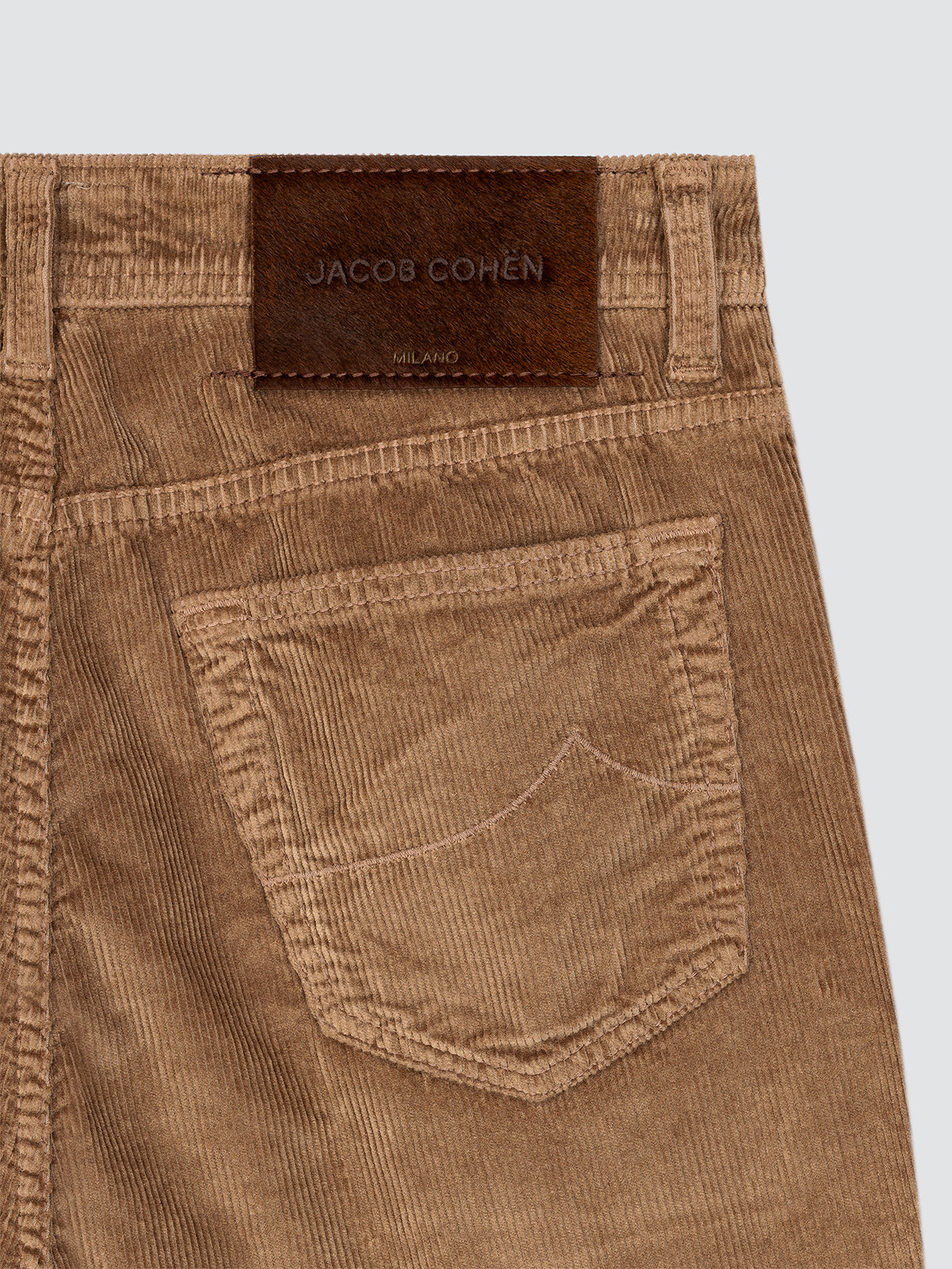 Close-up of brown corduroy pants with a brand label on a light gray background