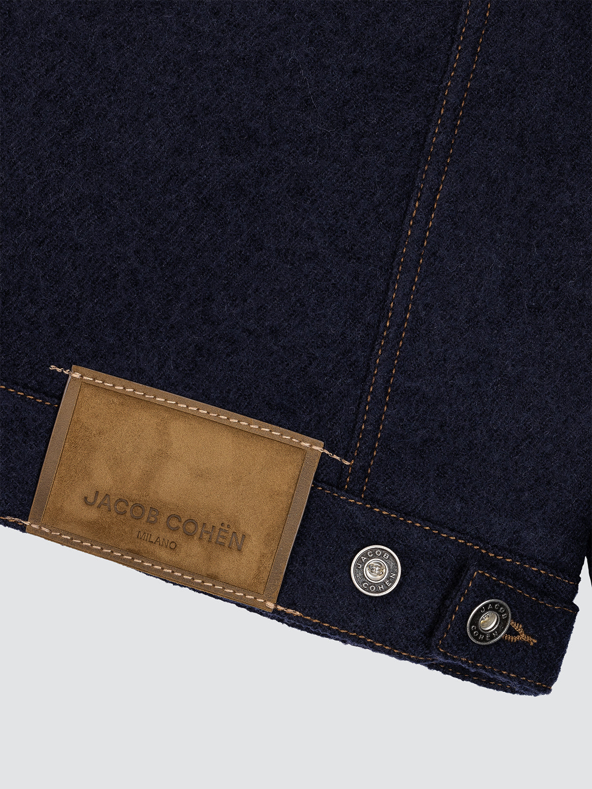 Close-up of a dark blue denim jacket with a brown label featuring 'Jacob Cohen' branding.