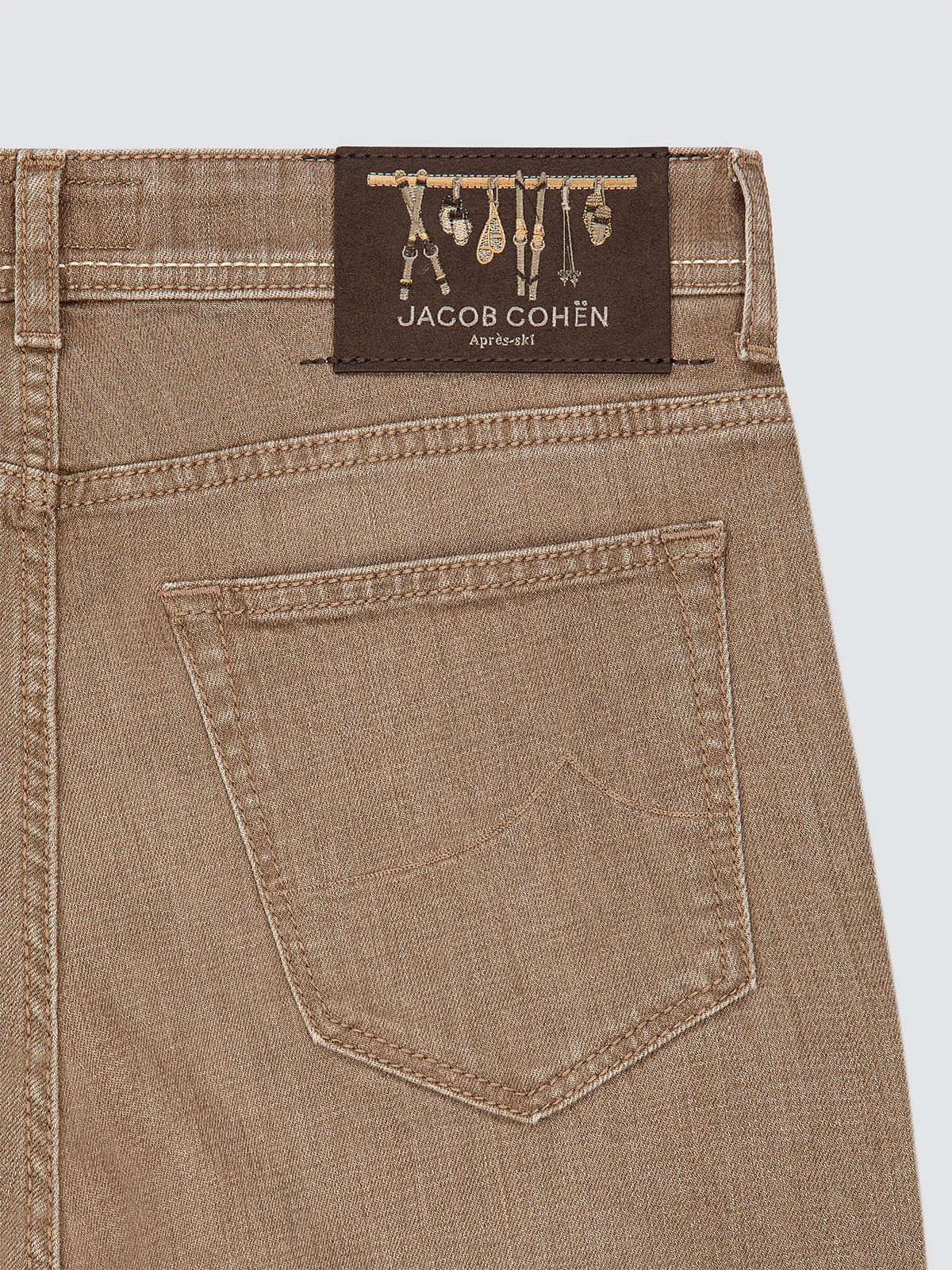 Close-up of beige jeans with a Jacob Cohen label on a light gray background