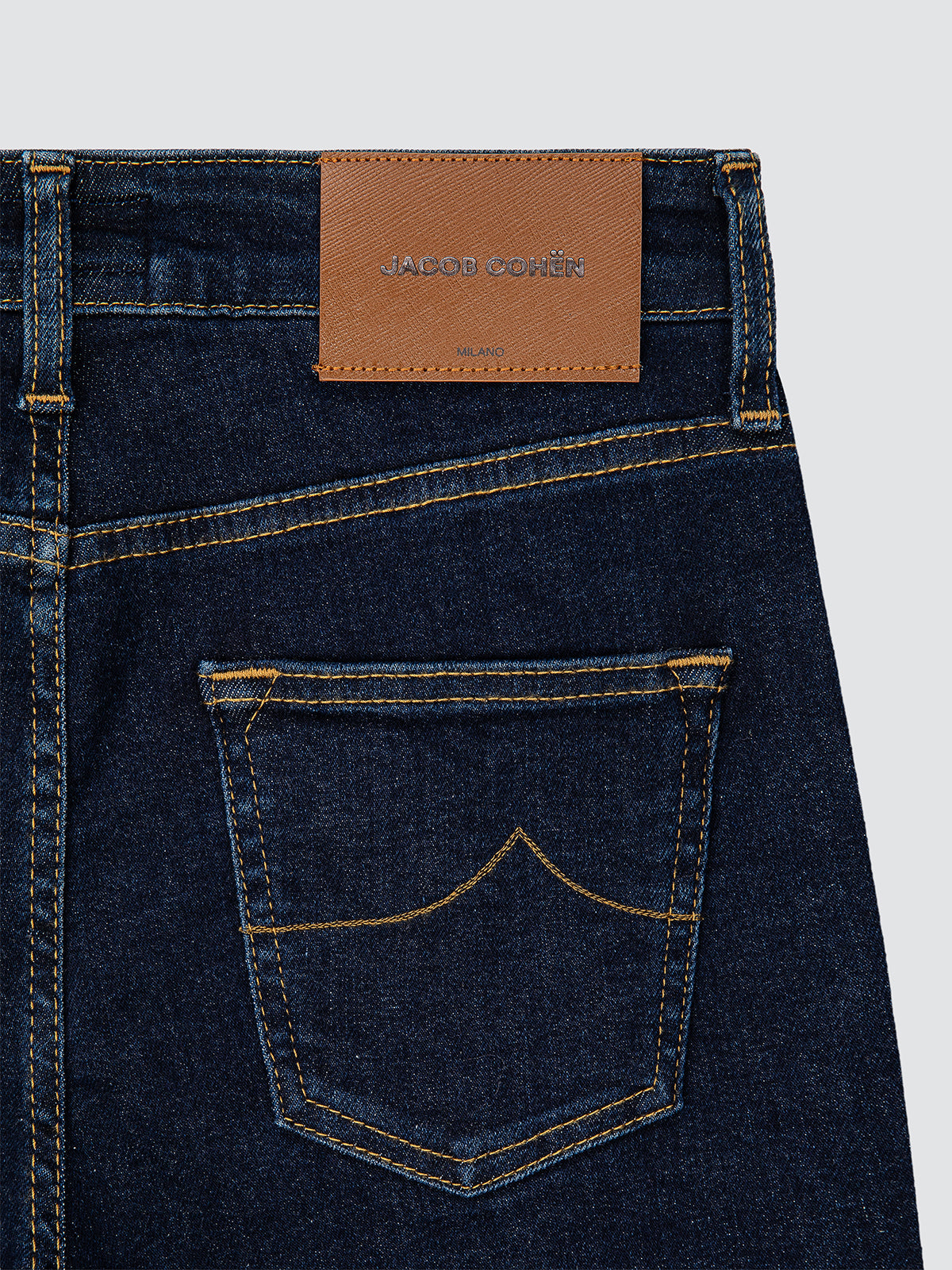 Close-up of dark blue jeans woman with a brown leather patch displaying 'Jacob cohen' brand on a light gray background.