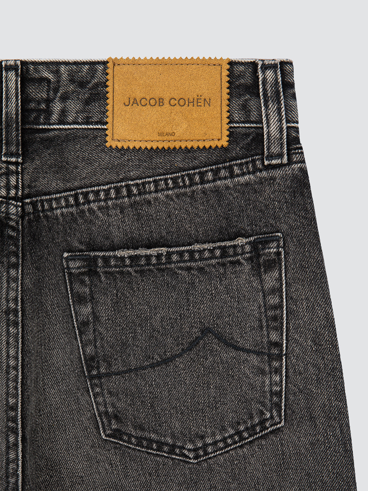 Close-up of black jeans with a Jacob Cohen label on a light gray background
