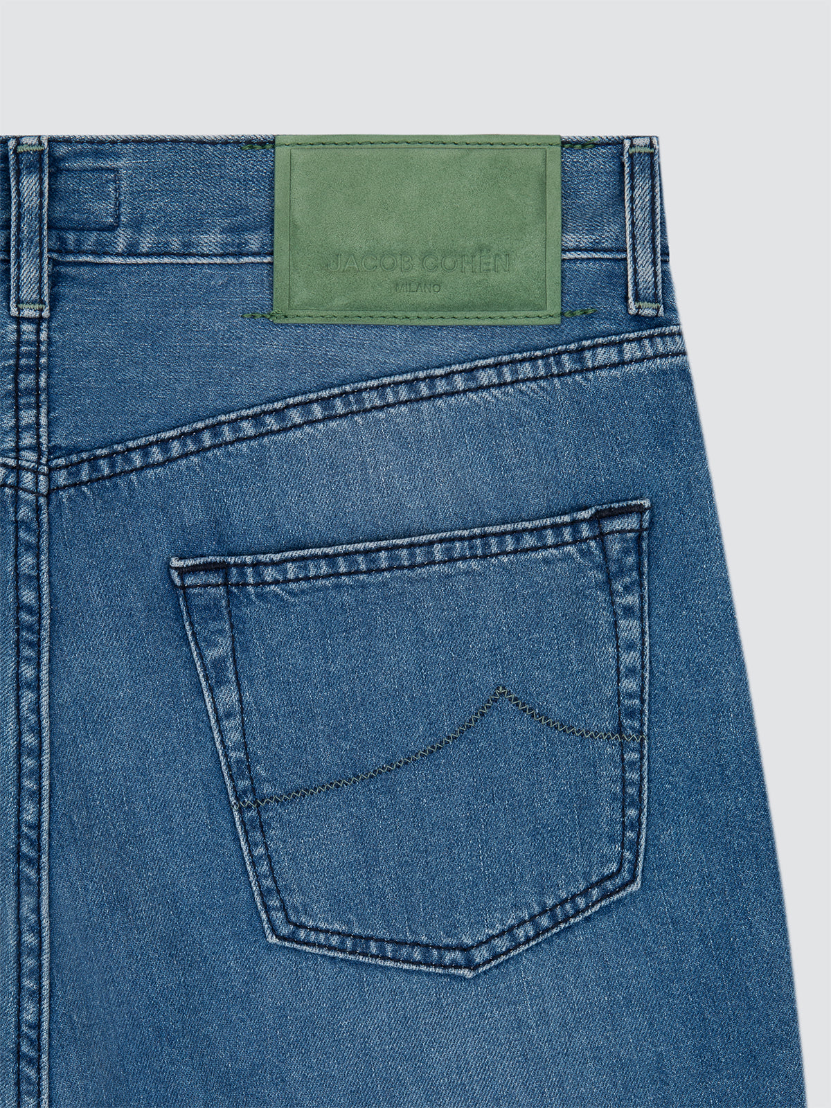 Close-up of blue denim jeans with a green label on a light gray background