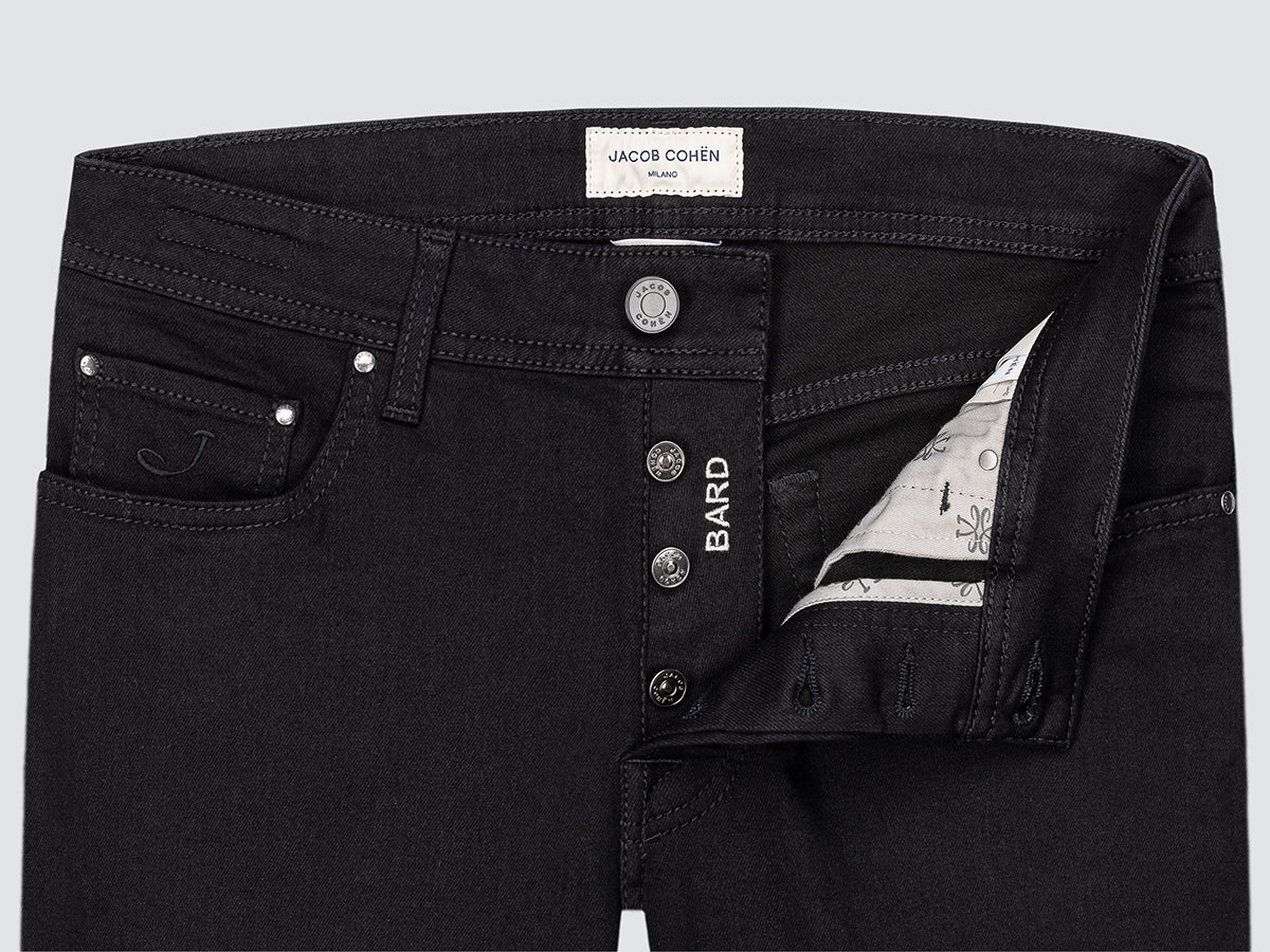 Close-up of black jeans with visible branding on a light gray background