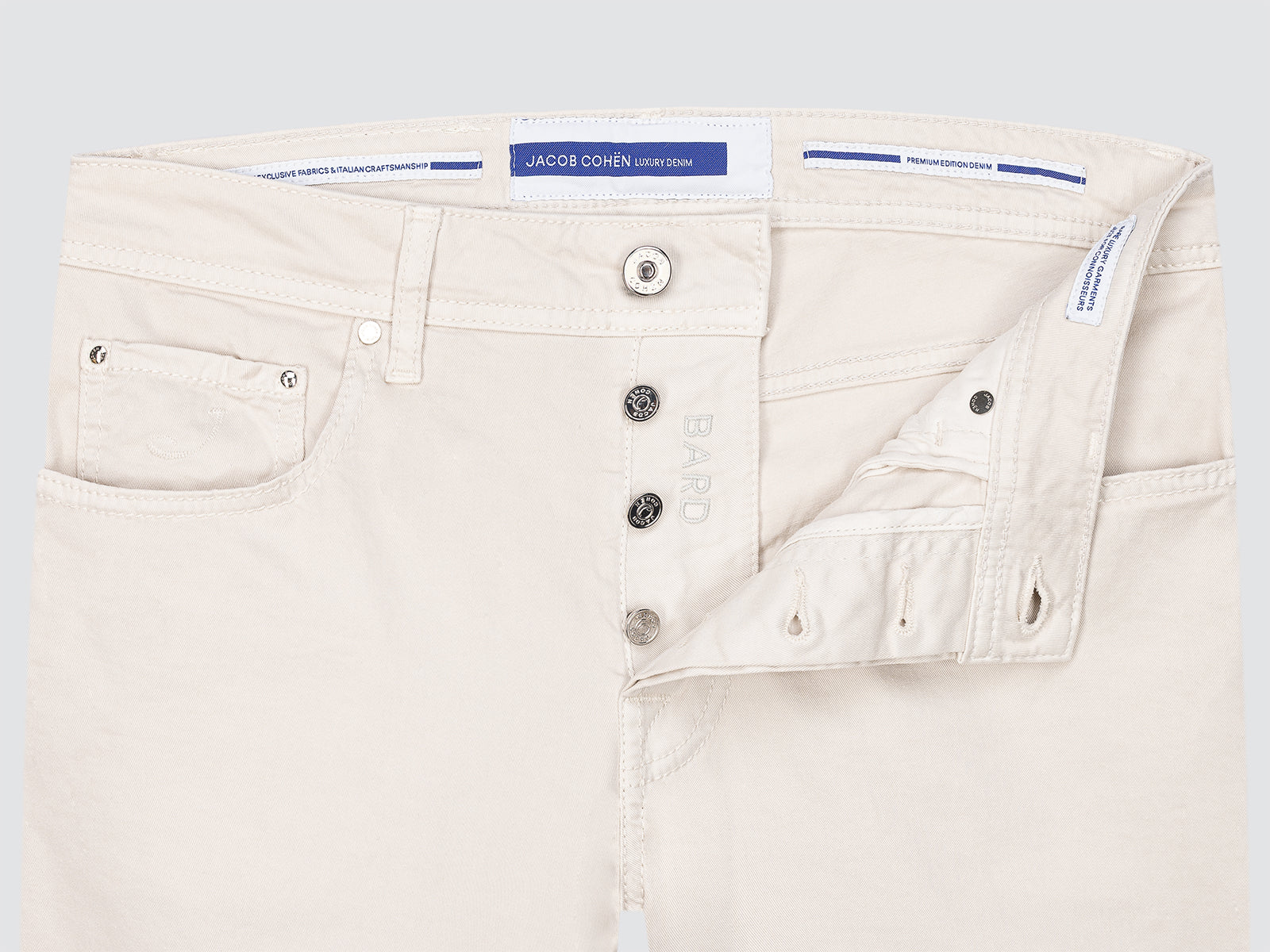 Close-up of beige twill chino jeans with brand label on a light gray background