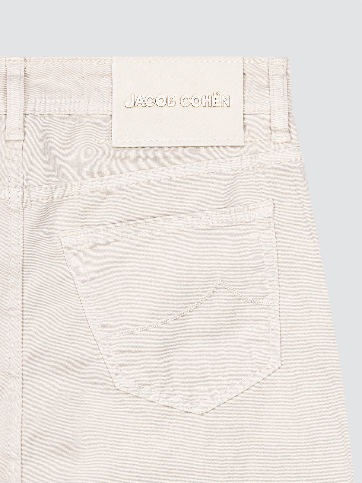 Close-up of a light-colored Twill 5 pocket with 'Jacob Cohen' branding on a light blue background.