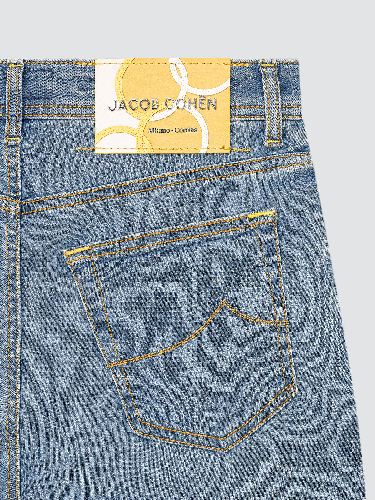 Close-up of blue jeans with a Jacob Cohen label yellow and white on a light gray background