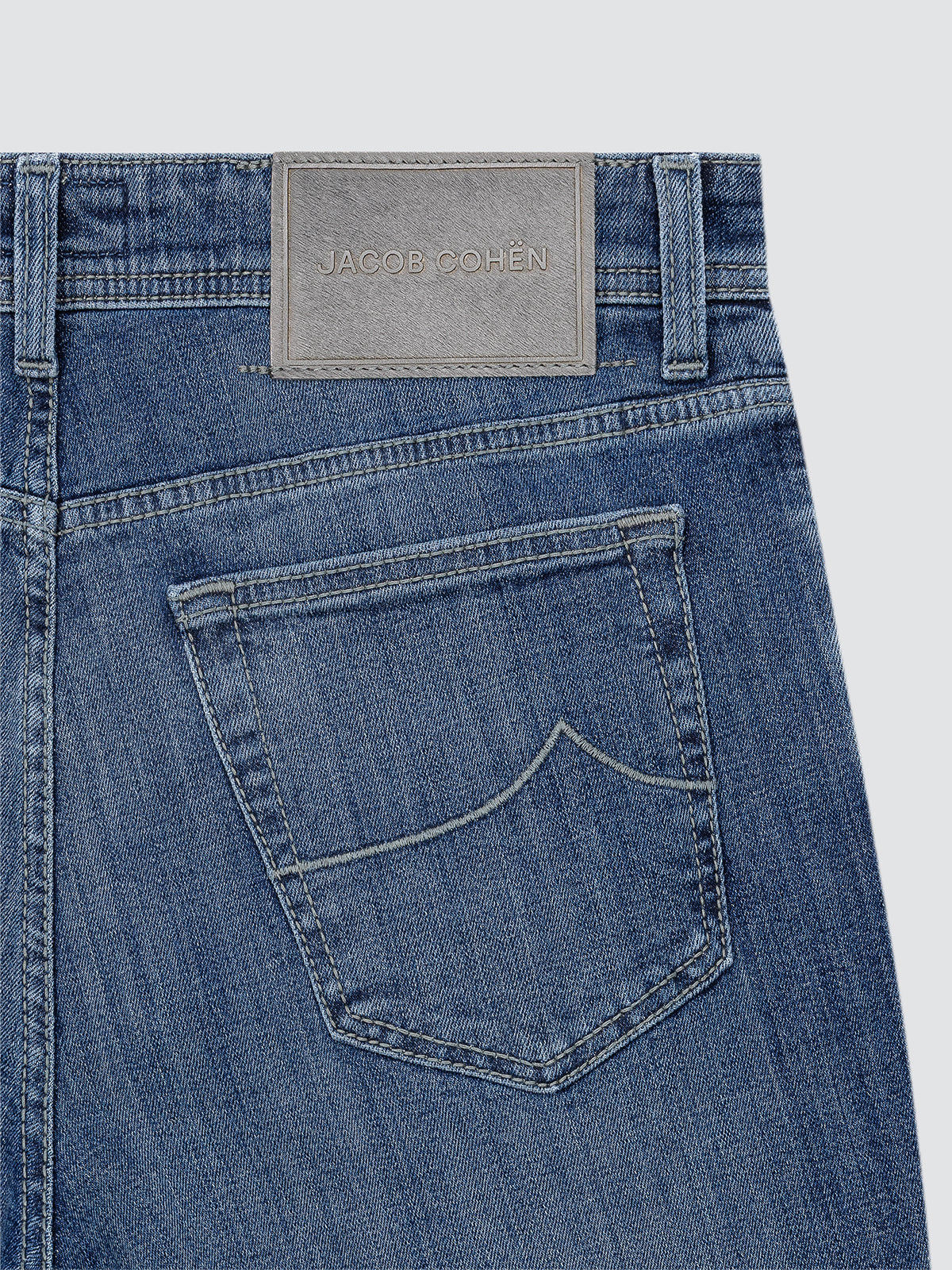 Close-up of blue jeans with a brand label on a light gray background BY JACOB COHEN