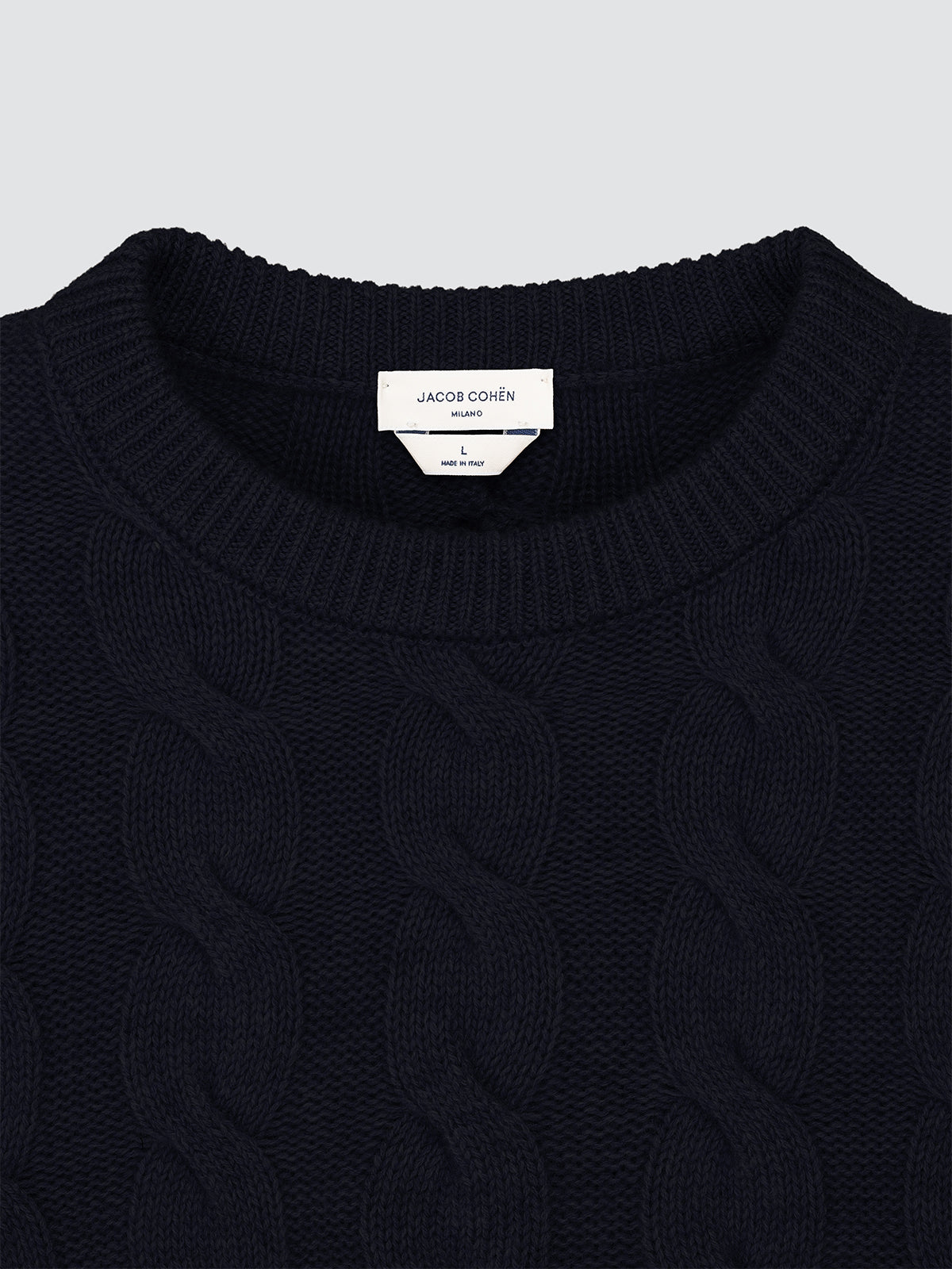 Close-up of a navy blue cable knit sweater with a brand label on a light gray background